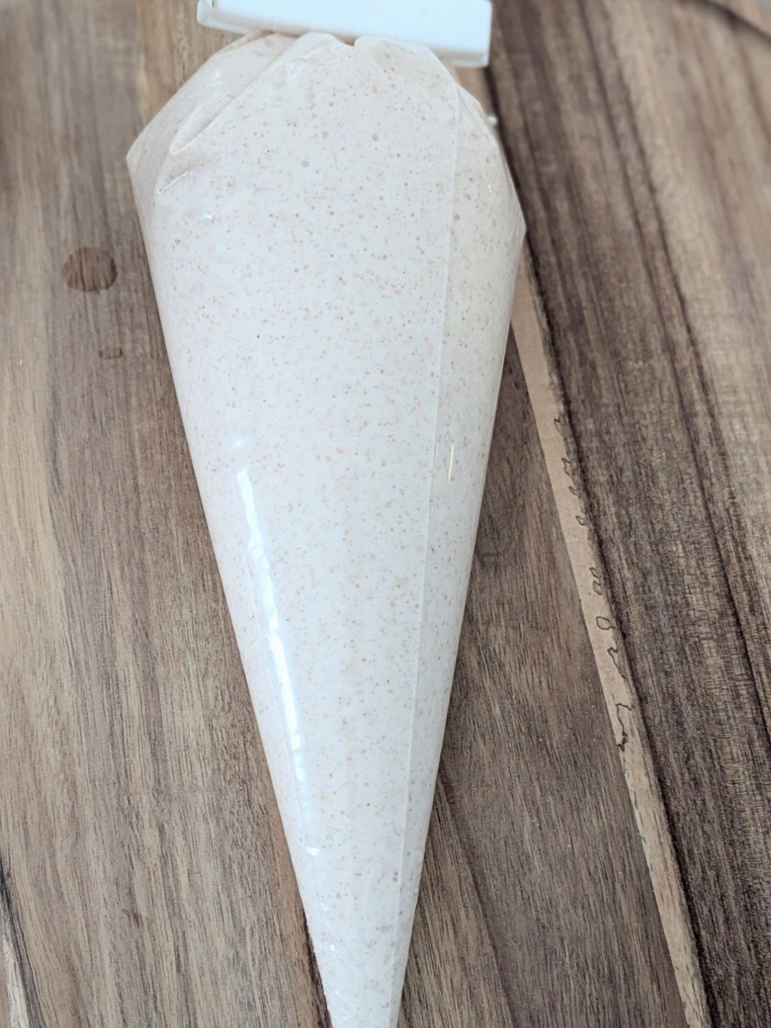 Piping bag filled with pancake mixture inside on a wooden surface. Background features earthy wood tones.