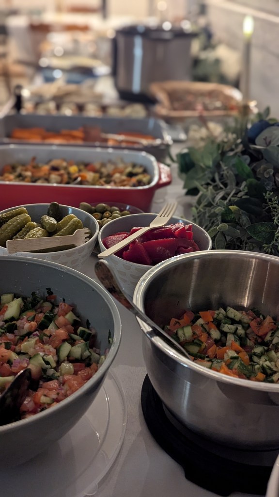 Colorful salads, casseroles, pickles, and veggies are displayed in bowls on a dining table with a leafy centerpiece under soft light, creating a cozy ambiance.