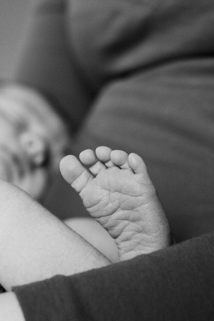 Close-up of a baby's foot in black and white, with the baby sleeping softly in the blurred background, creating a serene mood.
