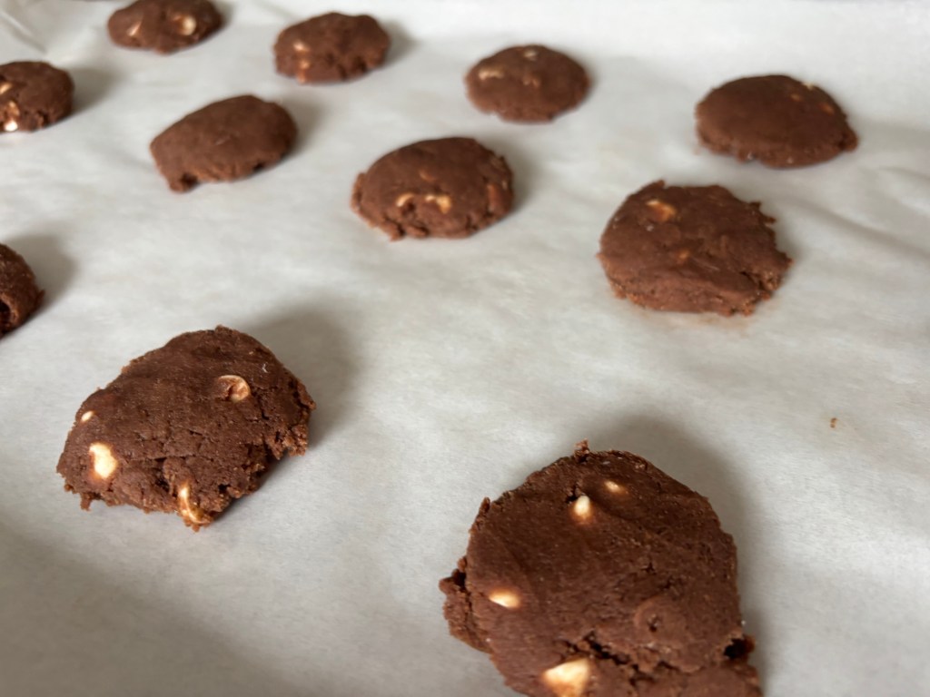 Chocolate cookies with white chocolate chunks on a baking sheet. Background is plain, creating a warm, homemade feel.