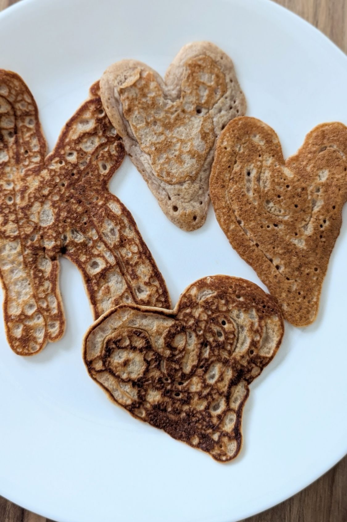 Heart-shaped pancakes on a white plate with wood table background, showcasing golden brown tones and a playful, homemade vibe.