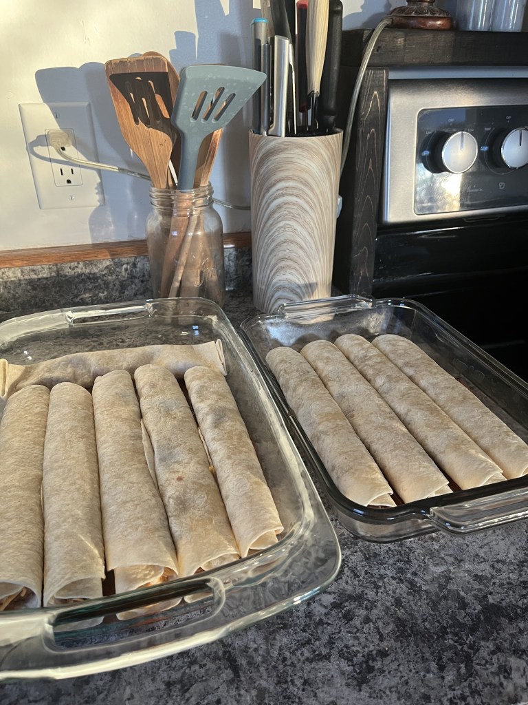 Glass dishes filled with rolled tortillas on a kitchen counter. Utensils in jars are in the background next to a stainless steel oven.