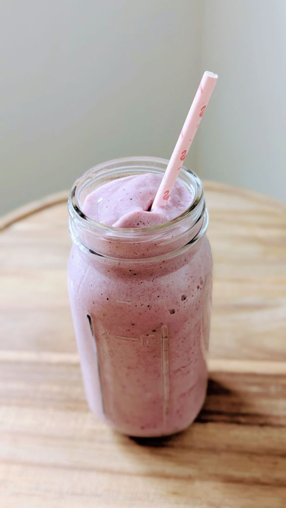 Pink smoothie in a glass jar with a pink straw, placed on a wooden table. The setting is bright and simple, creating a refreshing mood.