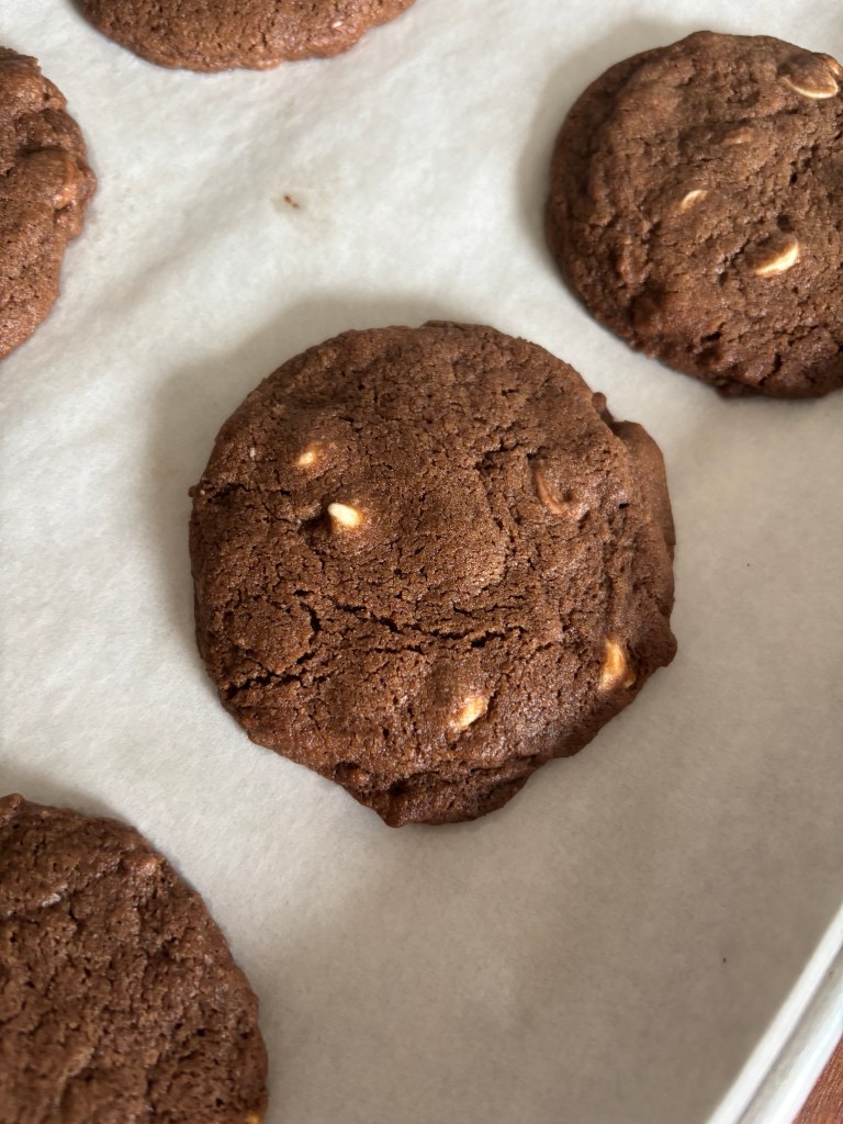 "Extreme Chocolate Chip" cookies with white chocolate chips on parchment paper. The cookies are round and brown, resting on a baking tray.