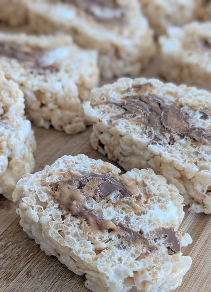 Rolled rice crispy treats with chocolate swirls on a wooden surface. The treats have a soft, textured appearance.