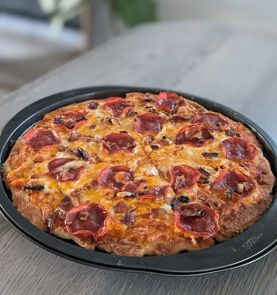 Pepperoni pizza with melted cheese on a black tray, on a wooden table. Background is softly blurred, creating a warm, appetizing mood.