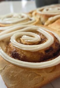 Close-up of freshly baked cinnamon rolls topped with cream cheese icing, showcasing their swirled design.