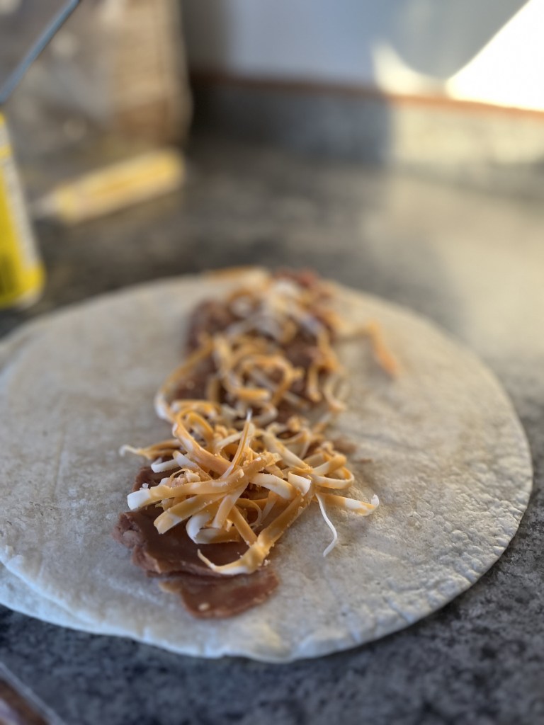 Tortilla with refried beans and shredded cheese on a dark countertop. Soft lighting creates a warm, inviting atmosphere.
