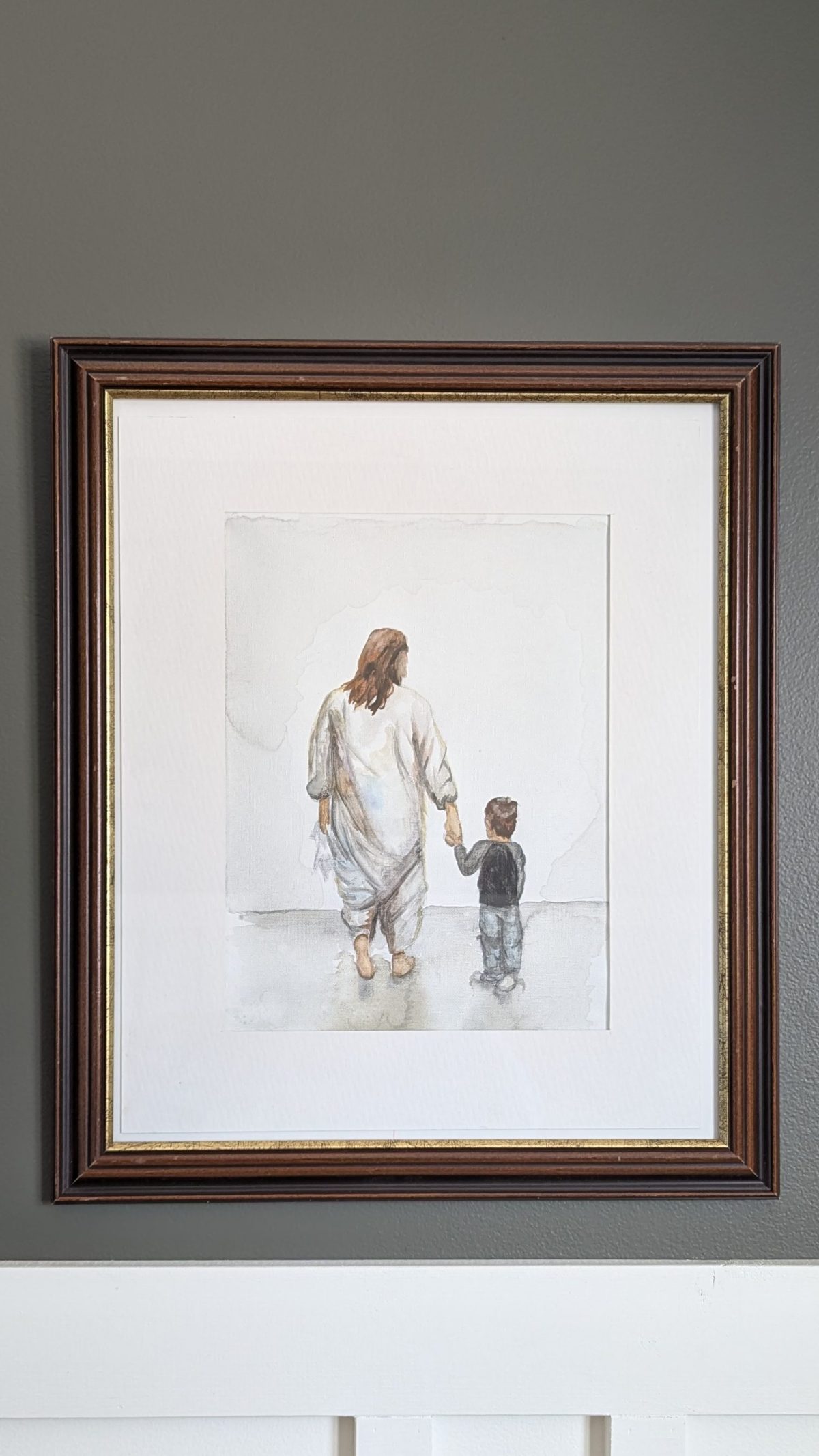 Painting of an adult in loose clothing holding a child's hand, walking away. Framed on a gray wall; soft, neutral tones convey warmth.