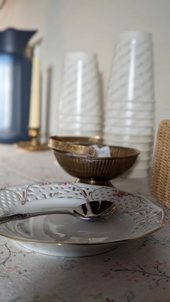 Elegant table setting with a decorative plate and spoon, gold-rimmed bowls, stacked white cups, and candles in a cozy, inviting atmosphere.