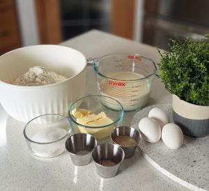Ingredients for cinnamon rolls including flour, milk, butter, sugar, eggs, and spices, displayed on a kitchen countertop.