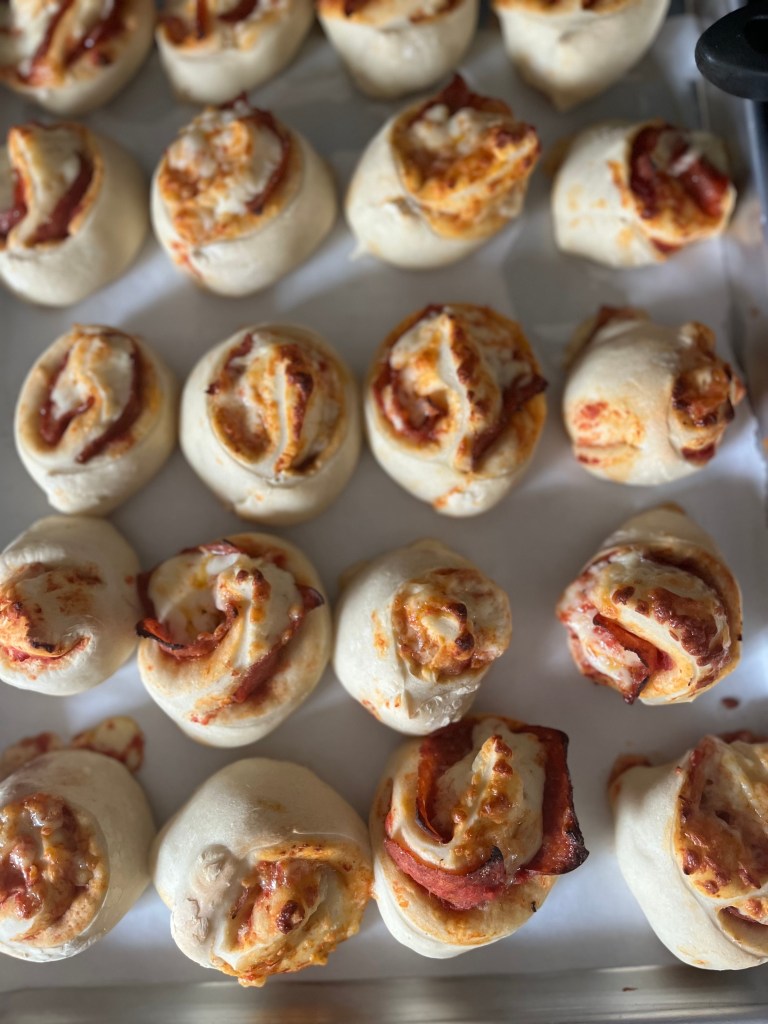Baked pizza rolls with browned cheese and pepperoni on white parchment paper in a metal tray, creating a fresh and inviting look.
