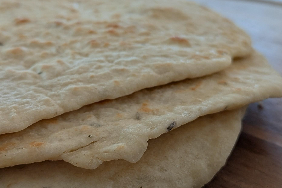 Close-up of three stacked flatbreads on a wooden surface, with a light brown, slightly textured appearance under soft lighting.
