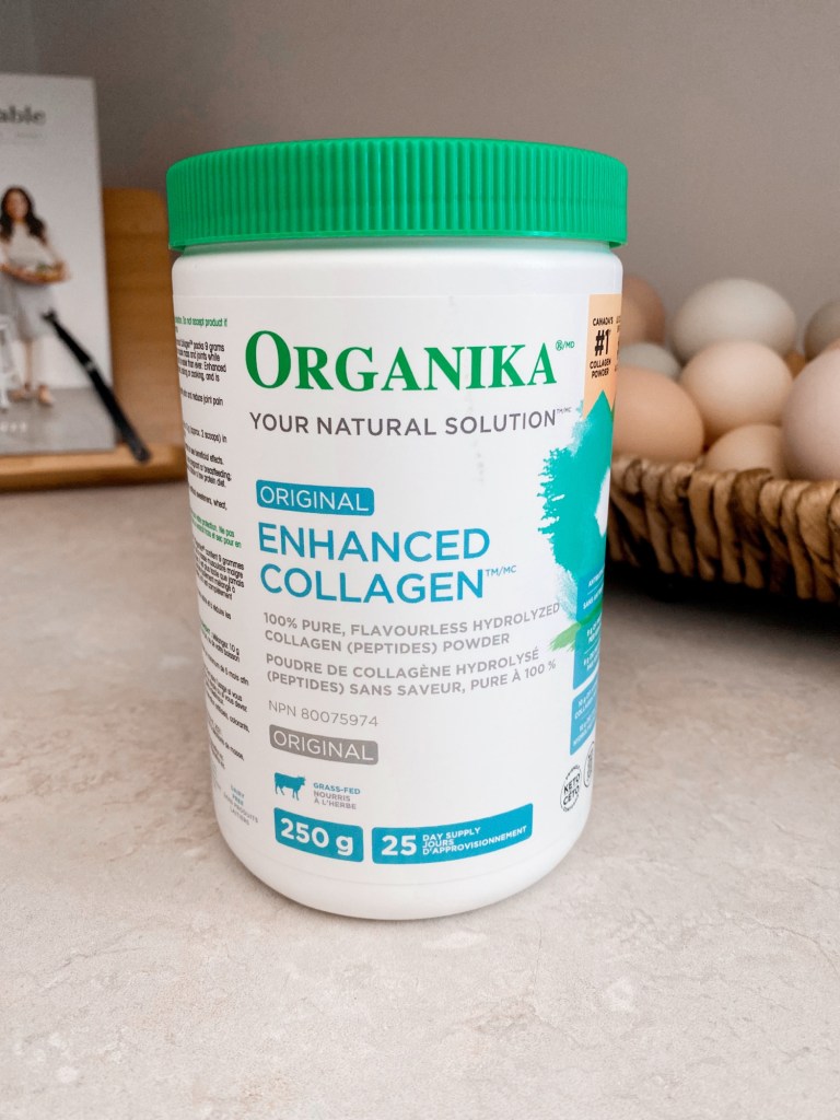 A container of Organika Enhanced Collagen powder with a green lid on a countertop, basket of eggs in the background.