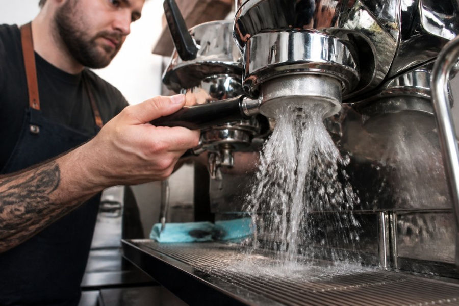 Barista using a blind portafilter to backflush and maintain commercial espresso machines in a cafe