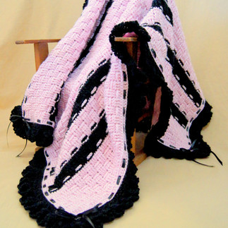 Light pink and black striped crocheted baby blanket with black ruffled edging.