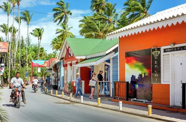 Colorful downtown street in Las Terrenas with local shops, restaurants, palm trees, and pedestrians.