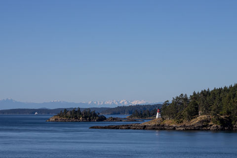 An island with a small lighthouse with mountains in the distance on a clear day