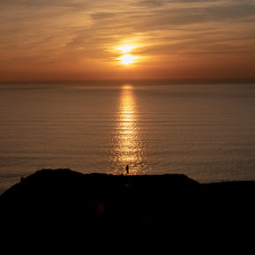 A person alone walking along the cliff silhouetted against an orange sunset