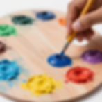 Artist's hand dipping a brush in blue paint for art classes near me.