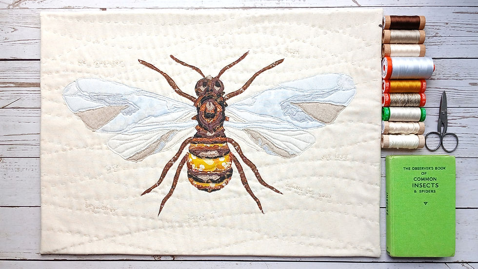 An art quilt of a bee with Aurifl threads, vintage book and scissors alongside it
