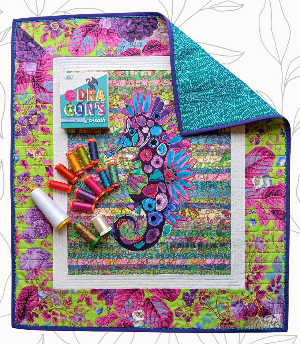 Quilted seahorse appliqué on layered fabric background with bubble stitching, framed with white and Kaffe Fassett borders. Aurifil threads displayed beside.
