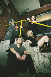 Avalon Stone and her band sit spread out on a grungy industrial staircase