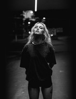 An alt rock girl stands in the shadows, with her face pushed up into the only light.