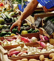 A hand reaching to grab a bell pepper amidst a vegetable stand.