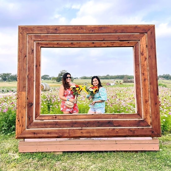Two young women in a large wooden photo frame by the Rockberry Ranch flower fields.