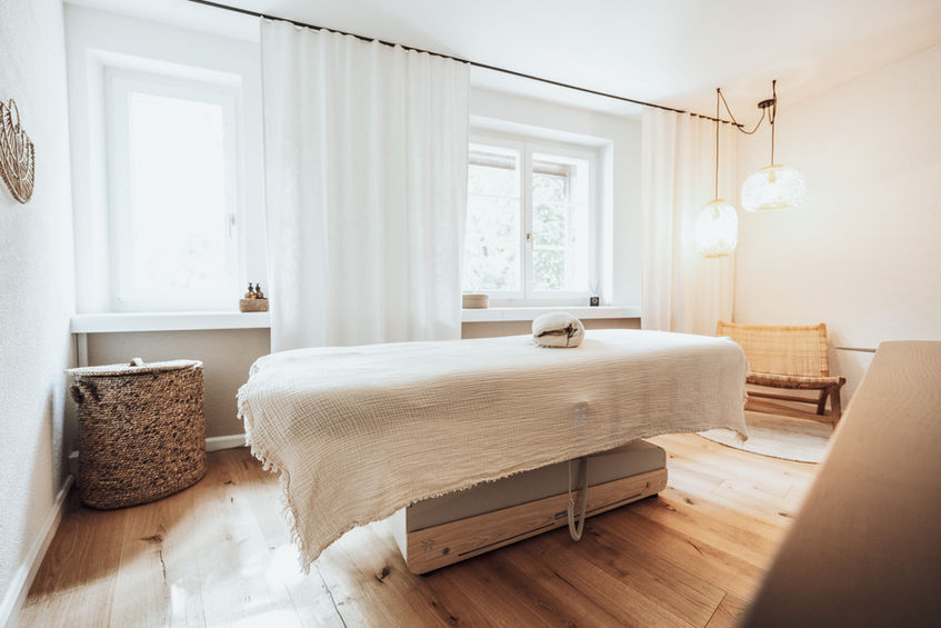 Massageliege mit cremefarbener Musselin-Decke im hellen misalus Behandlungsraum in Baden