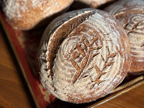 A round loaf of gluten-free bread, scored with a stem-and-leaf design