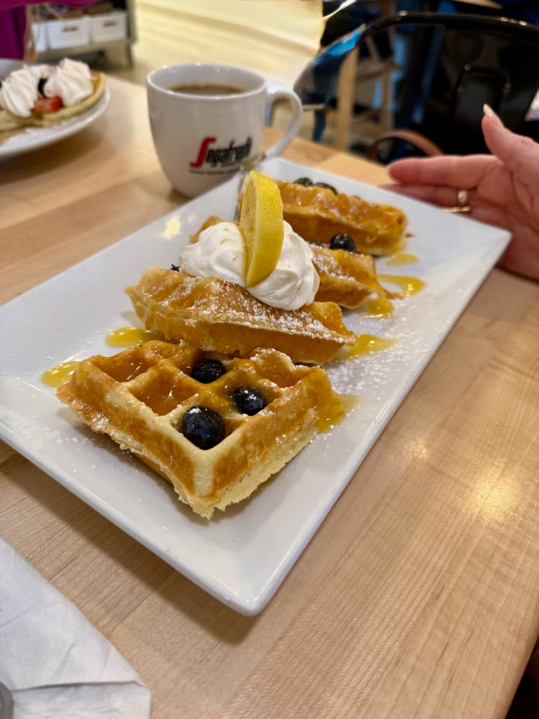 Gluten-free lemonberry waffles on a white plate with whipped cream and a slice of lemon on top