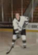 Dave Chaney in his hockey uniform, smiling and posing with his hockey stick
