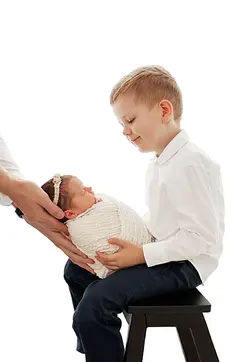 Großer Bruder hält sanft sein neugeborenes Geschwisterchen - Geschwisterfotos Hamburg