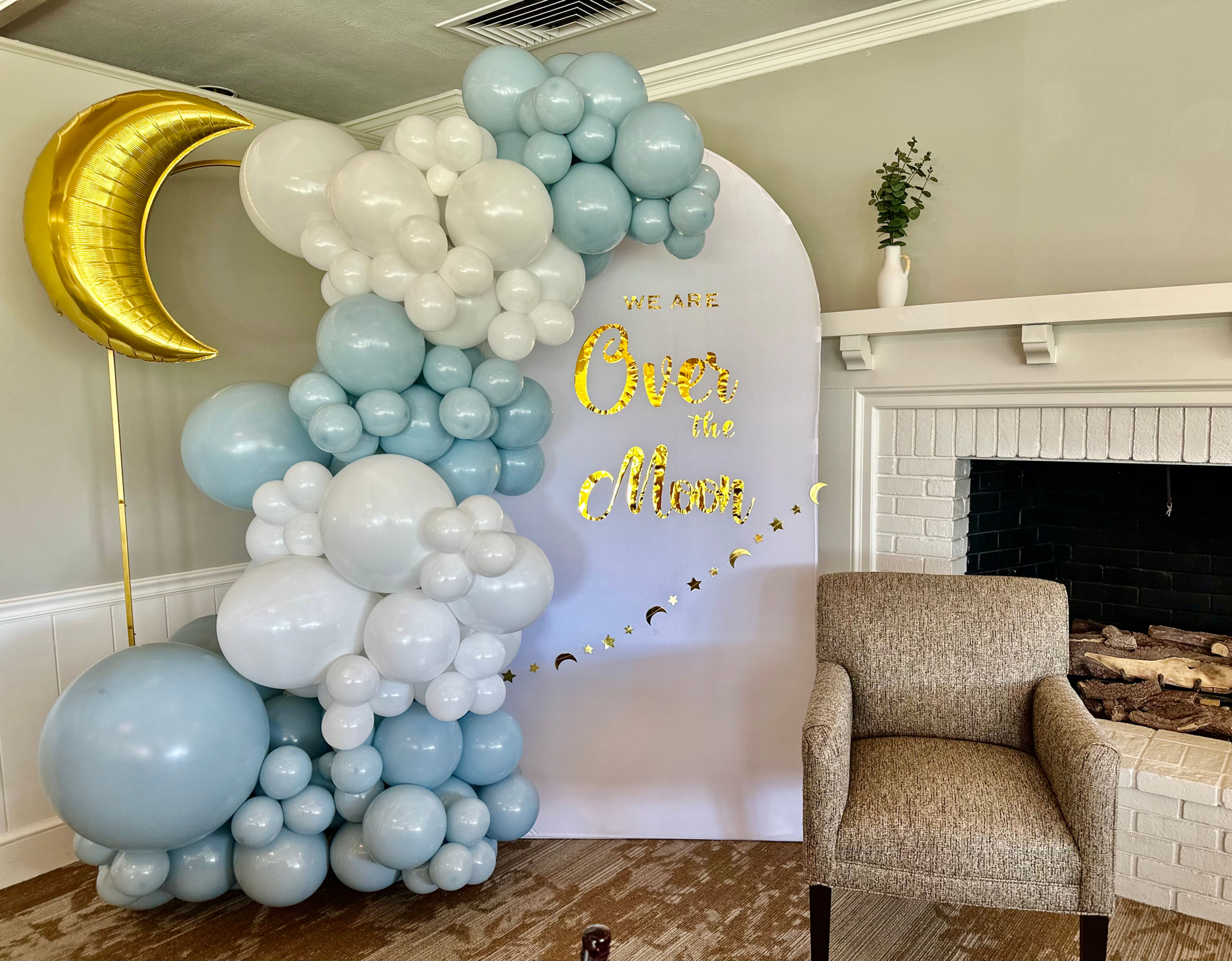 Balloom garland. Colors: baby blue, white. White backdrop with "we are over the moon" and a golden moon mylar balloon