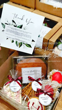 Elegant customised baby full moon gift box by CORALS Catering featuring a personalised thank you card, traditional bright red egg symbolising happiness and good fortune, orange butter cake, royal icing cookies, marshmallows, pretzel sticks, and premium kraft gift box packaging for newborn celebrations in Malaysia.