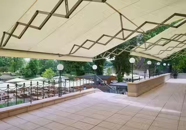 Blick auf die mit großen Markisen überdachte Terrasse des Zenner, ausgestattet mit Tischen und Bänken.