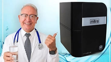 Yaşlı ve uzman doktor, el ile başparmak işareti yaparak tavsiye ettiğini su arıtma cihazını gösteriyor.