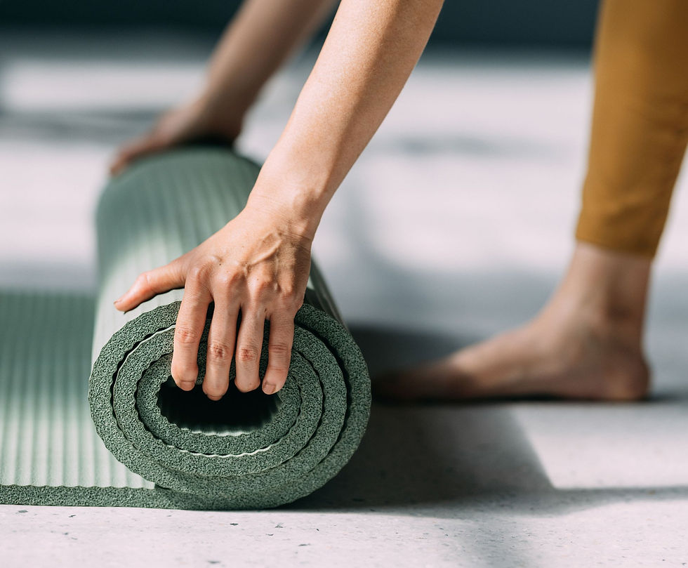 Person rolling up a green yoga mat on a light-colored floor after a workout or yoga session.