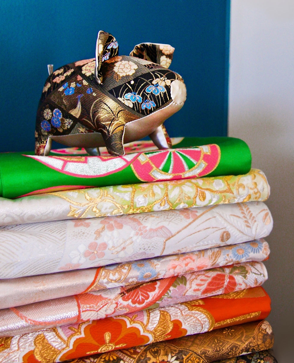 Buta the Kimono Pig sitting atop a mountain of fukuro obi in the Arashi House studio.