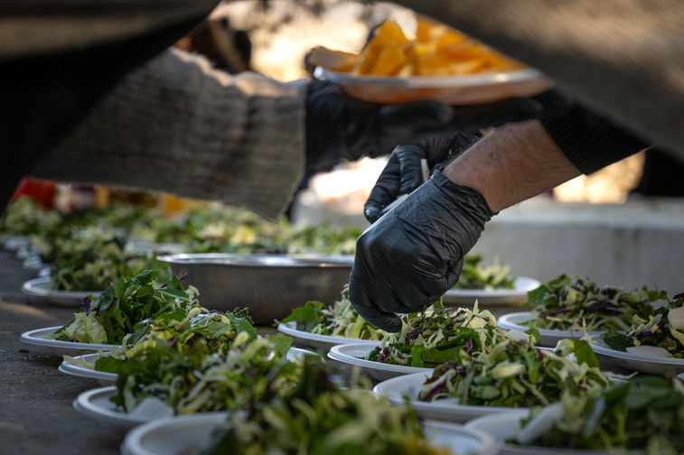 Chef hands preparing fresh salads in outdoor kitchen, Antonis Karakonstantakis photographer, food plating process, catering preparation, gloved hands assembling dishes, fresh vegetables plates, commercial kitchen workflow, organized food production, culinary precision, hospitality kitchen scene