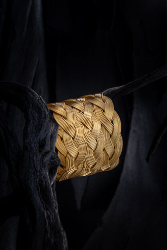 Crete, jewelry photography with studio lighting, gold woven bracelet with intricate texture on dark artistic background, luxury product photography for jewelry brands and e-shop, branding image with strong contrast and premium aesthetic, φωτογράφιση κοσμημάτων στην Κρήτη για κατάλογο και επαγγελματική προβολή προϊόντων