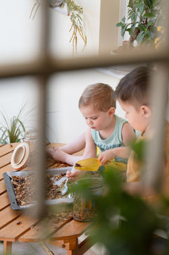 Two young children playing together during a lifestyle family photography session in Crete, captured through a window frame in natural light.