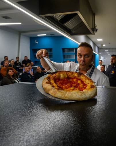 Chef presenting a freshly baked pizza to an audience during a live cooking demonstration, professional event photography capturing real interaction, Antonis Karakonstantakis photographer, culinary event, gastronomy experience, chef in action, food presentation moment, audience engagement, live cooking performance, hospitality event documentation