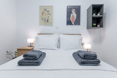 Professional interior photograph of a modern bedroom with a double bed, neatly folded towels, bedside lamps, contemporary wall art, and minimalist décor for hotel, Airbnb, or real estate marketing.