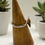 Thumbnail: the side view of silver ring with raised, texture circular design displayed on a wooden cone, with two small succulent plants