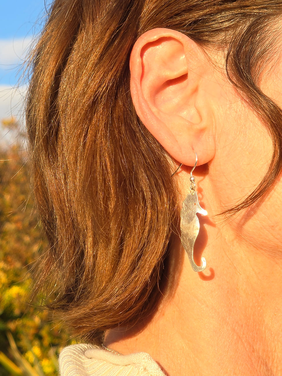 Thumbnail: Silver seahorse shaped earrings being worn
