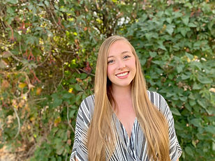 Savanna stands in front of a wall of leaves, hair down and smiling