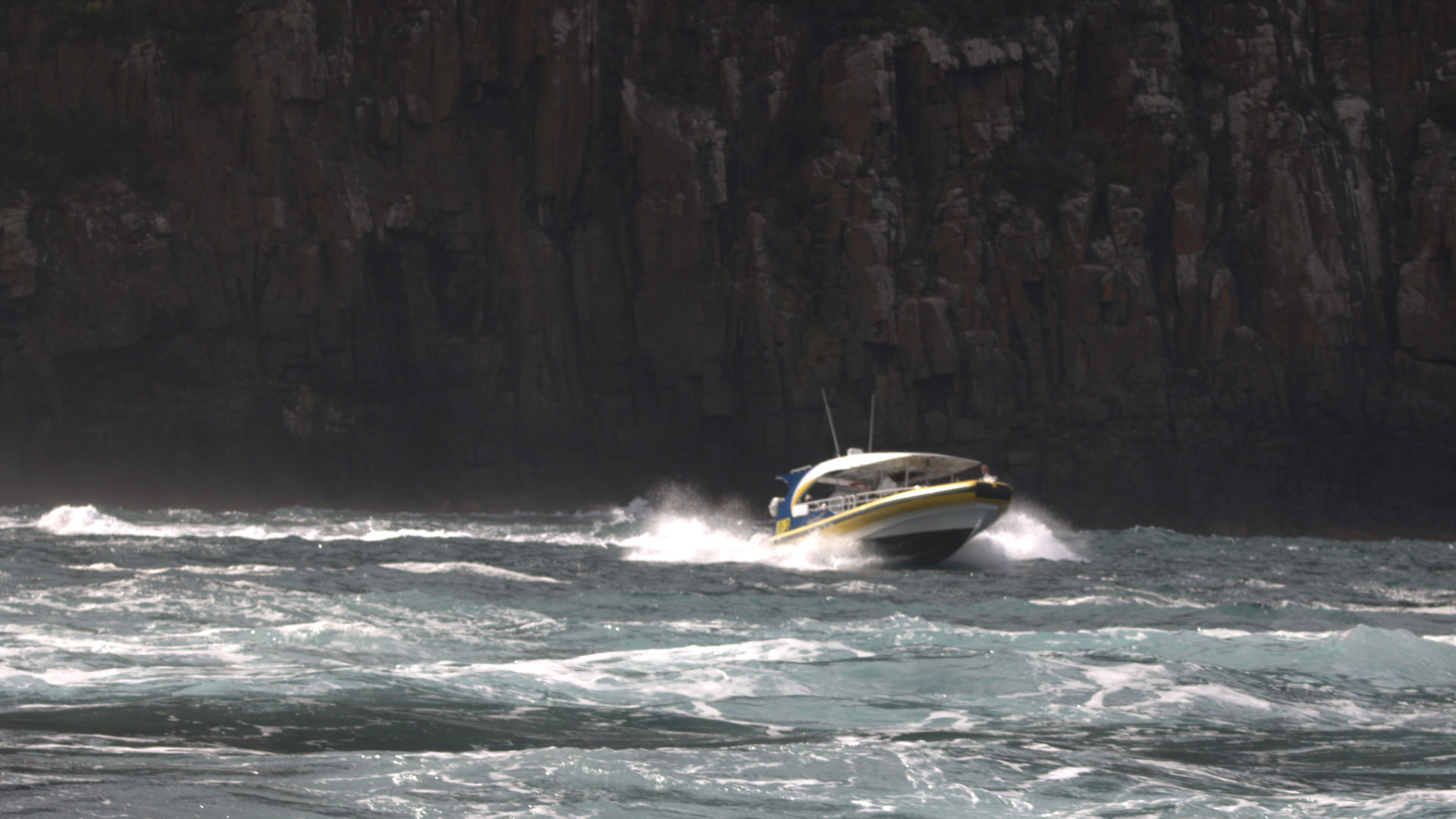 A boat speeding away from sea cliffs